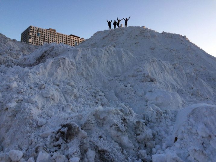 Students standing atop giant snow pile on west campus