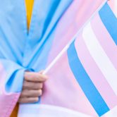 Person wearing blue and pink striped clothing and holding blue, pink, and white striped flag