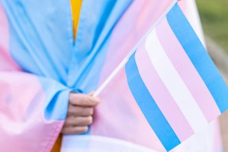 Person wearing blue and pink striped clothing and holding blue, pink, and white striped flag